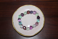 a tumbled fluorite crystal bracelet with purple blue red green beads on a pink plate with gold trim on wood board
