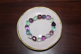 a tumbled fluorite crystal bracelet with purple blue red green beads on a pink plate with gold trim on wood board
