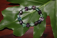 a tumbled fluorite crystal bracelet with purple green and blue beads on a green leaf