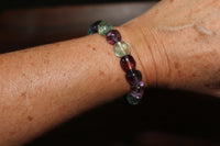 a purple green blue and red bead tumbled fluorite crystal bracelet on a woman's wrist