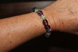a purple green blue and red bead tumbled fluorite crystal bracelet on a woman's wrist