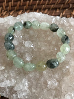 a light green tumbled prehnite crystal stretch bracelet on a white apophyllite crystal set on top of a wicker tray