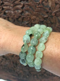 3 light green with dark inclusions of tumbled prehnite crystal stretch bracelets on a woman's arm against a carved indian wood board